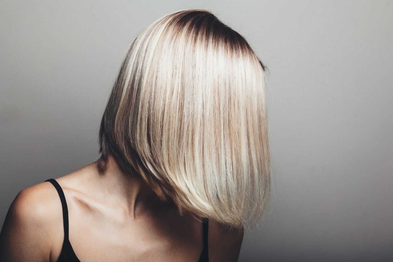 Short-haired person with blonde bob hairstyle against a grey background.
